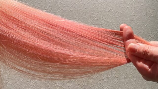 美容師さんがピンク色に染めた髪の毛を手にとって色の確認をしている写真